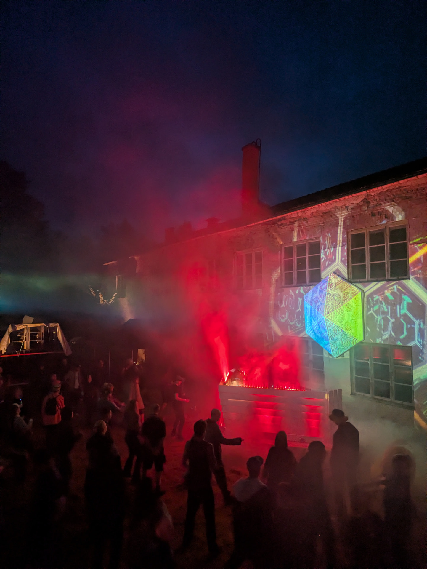 Festivalbesökare framför en tegelbyggnad med geometriska ljusprojektioner och röd scenbelysning nattetid