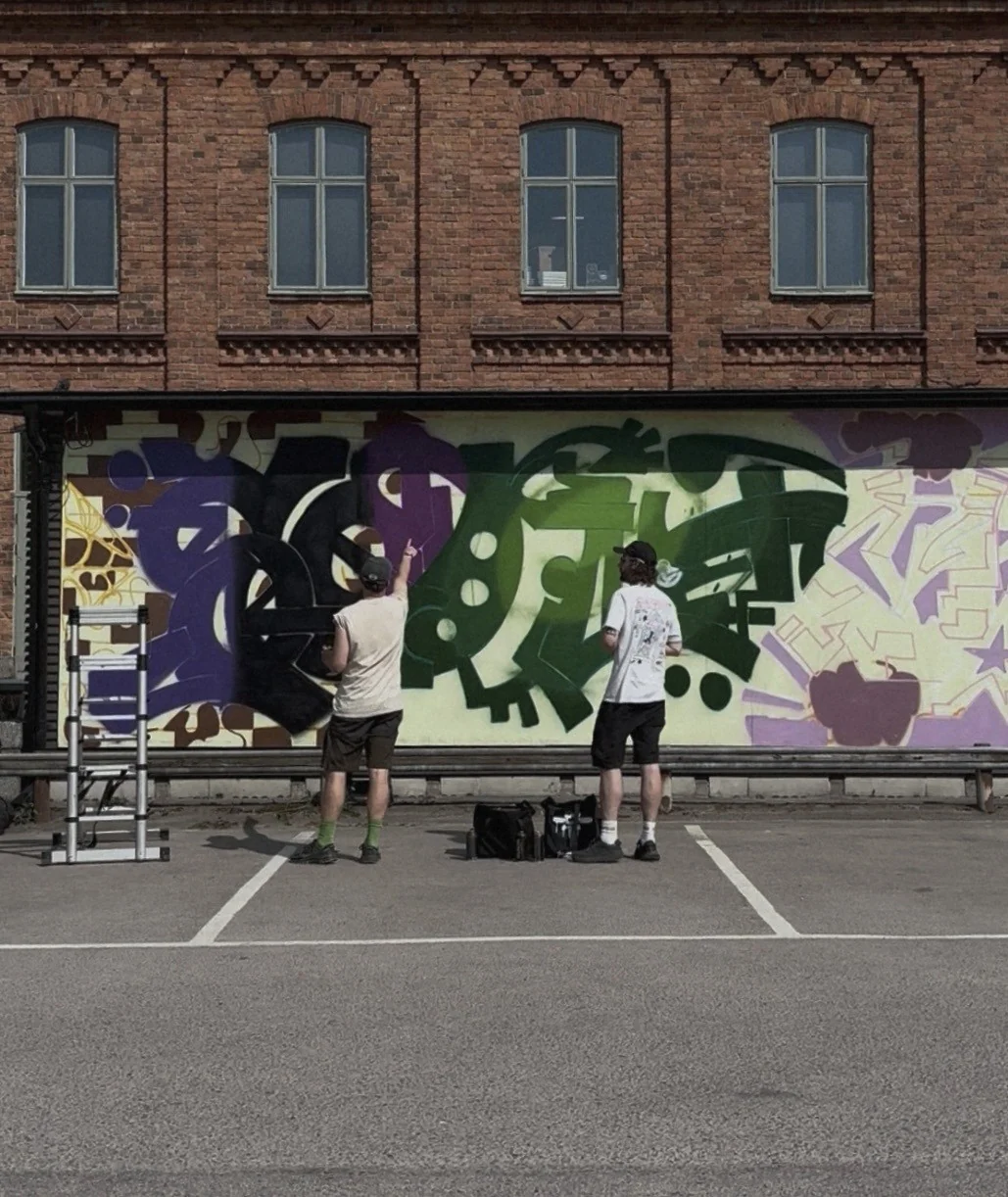 Två konstnärer målar muralen Lager på lager på en lång vägg