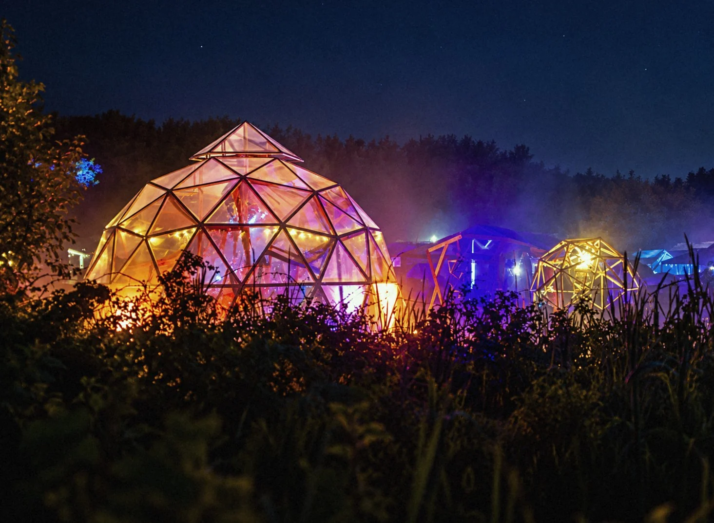 Upplysta domer av trä och plast i dimma på festivalområdet nattetid