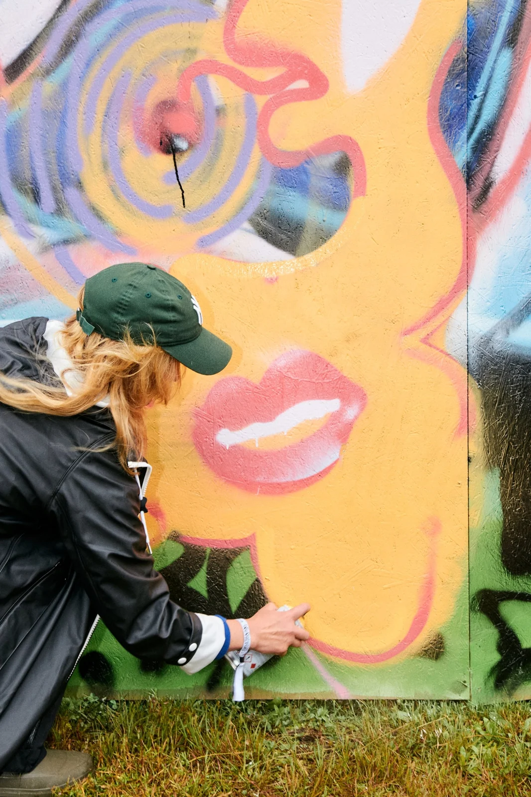 En besökare sprayar på ett stort målat ansikte på väggen, sedd bakifrån