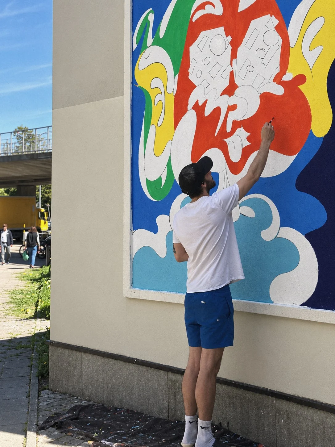 Konstnären målar en färgstark figurativ mural på en husfasad